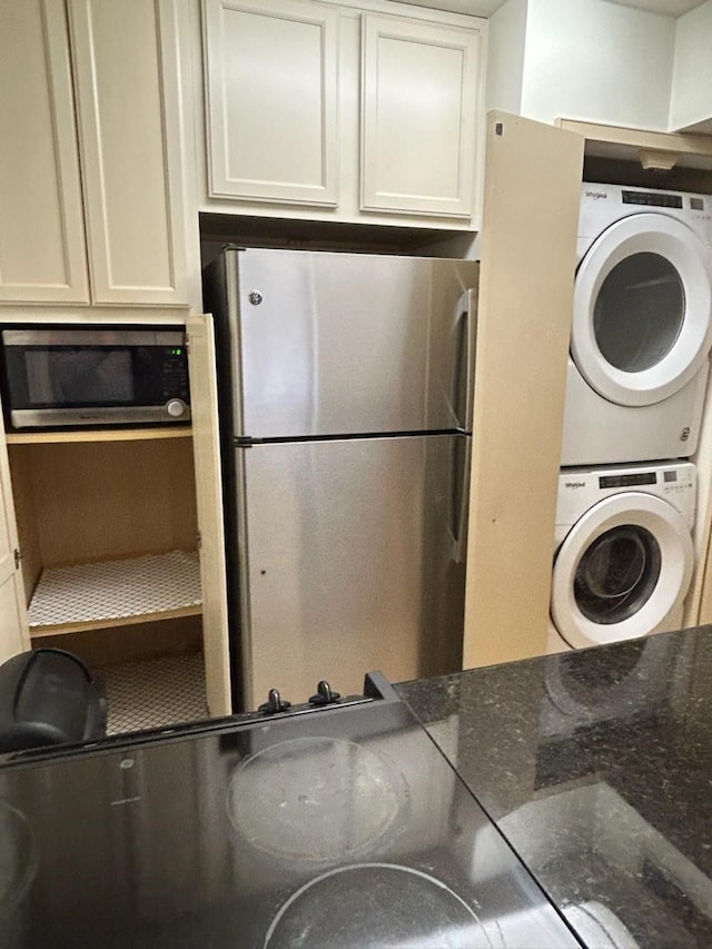 kitchen featuring white cabinets, appliances with stainless steel finishes, stacked washer and dryer, and dark stone counters