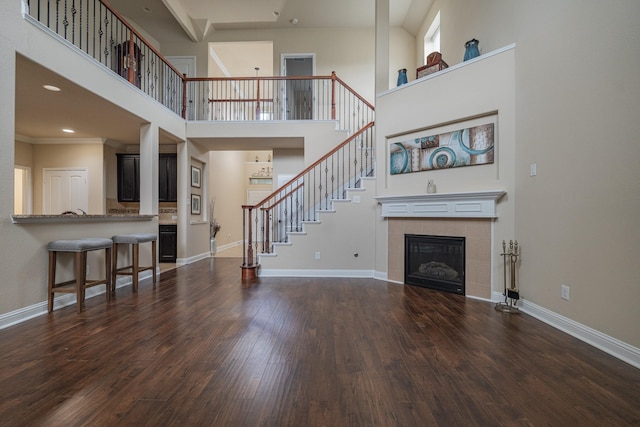 living room with crown molding, a towering ceiling, dark wood-type flooring, and a tiled fireplace