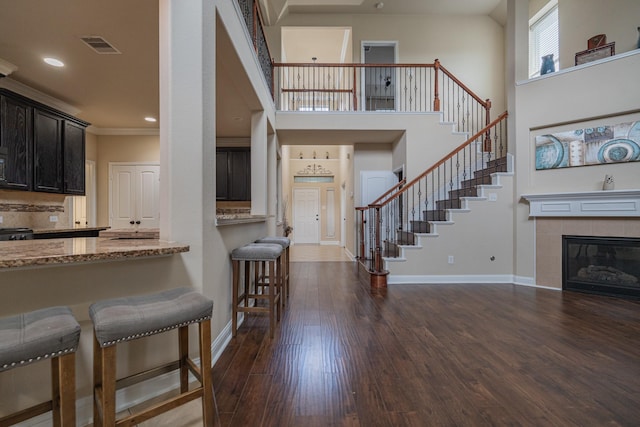 entrance foyer with a tiled fireplace, crown molding, dark wood-type flooring, and a high ceiling