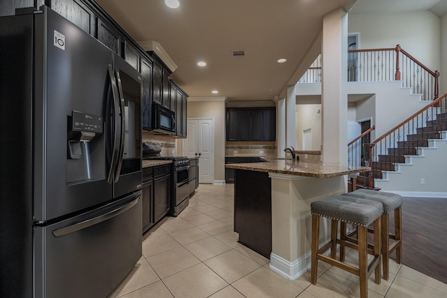 kitchen with black appliances, decorative backsplash, light stone countertops, light tile patterned floors, and a breakfast bar area