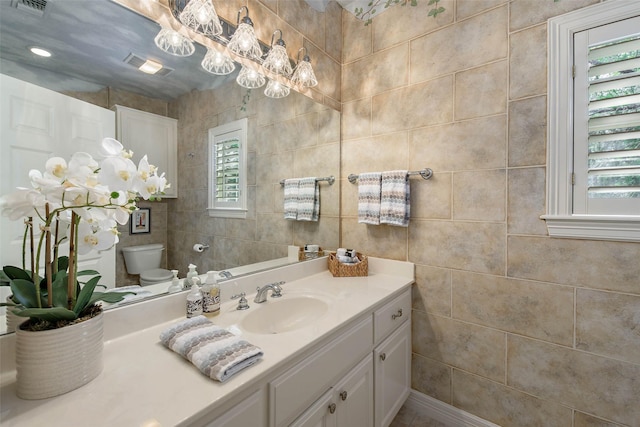 bathroom featuring vanity, toilet, plenty of natural light, and tile walls