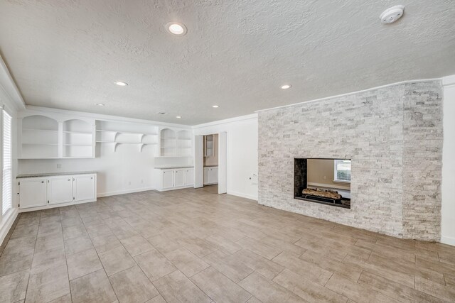 unfurnished living room with a stone fireplace, built in features, a healthy amount of sunlight, and a textured ceiling