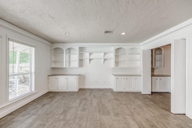 interior space with white cabinets, a textured ceiling, and light hardwood / wood-style flooring