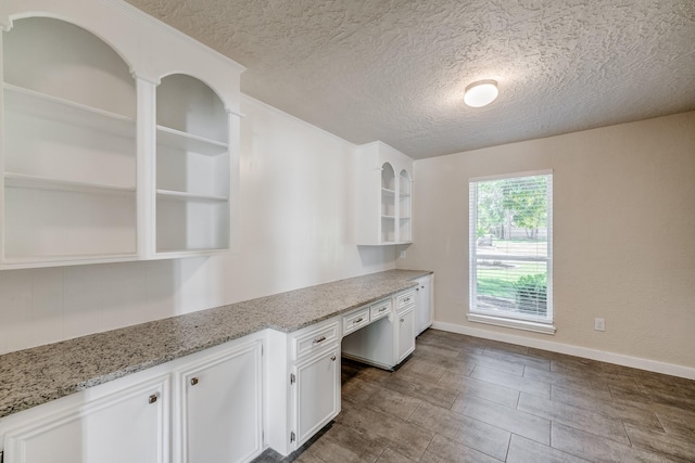 kitchen with white cabinets, a textured ceiling, built in desk, and light stone counters