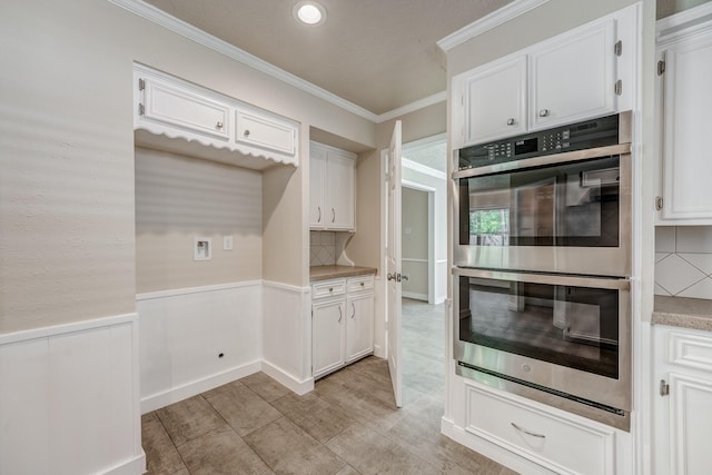 kitchen with white cabinets, crown molding, stainless steel double oven, and backsplash