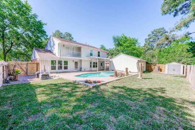 rear view of property featuring a fenced in pool, a balcony, a yard, a storage unit, and a patio area