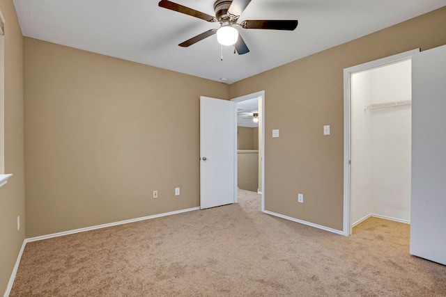 unfurnished bedroom featuring a walk in closet, ceiling fan, a closet, and light carpet