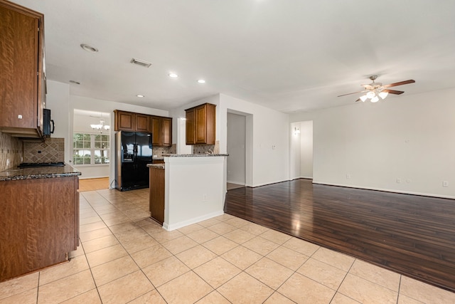 kitchen with black appliances, ceiling fan with notable chandelier, light hardwood / wood-style flooring, decorative backsplash, and dark stone countertops