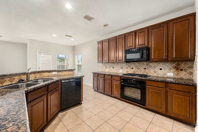 kitchen with sink, dark stone counters, decorative backsplash, light tile patterned flooring, and black appliances