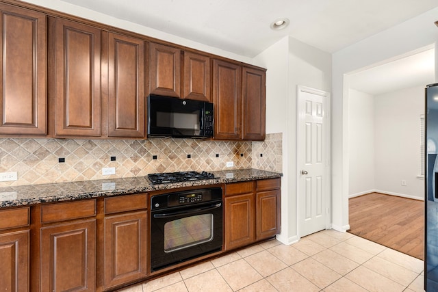 kitchen with dark stone counters, decorative backsplash, light tile patterned flooring, and black appliances