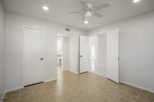 unfurnished bedroom with light tile patterned floors, a closet, ensuite bathroom, and ceiling fan