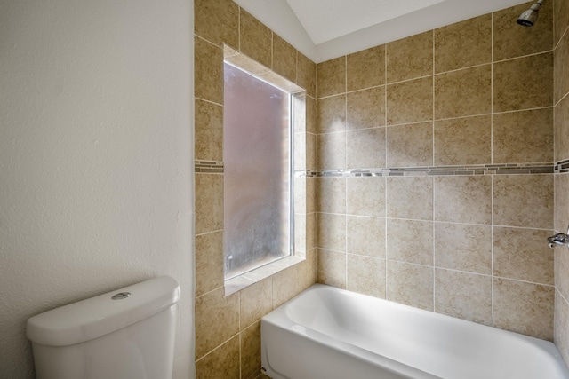 bathroom featuring toilet, tiled shower / bath, and vaulted ceiling