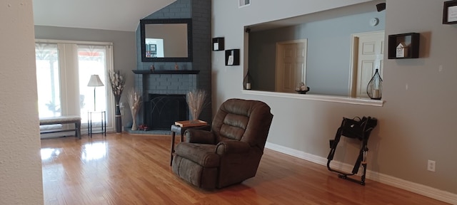 sitting room with hardwood / wood-style flooring, lofted ceiling, and a brick fireplace