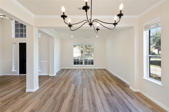 unfurnished living room with light hardwood / wood-style floors, crown molding, a wealth of natural light, and an inviting chandelier