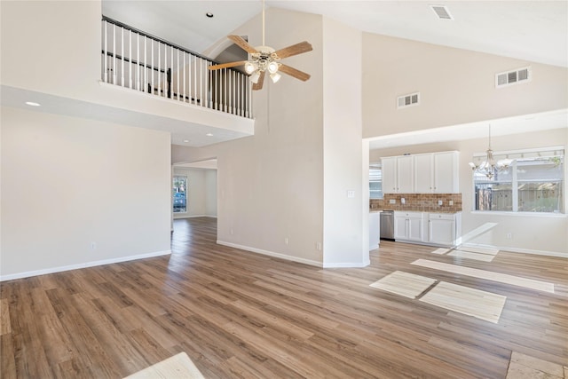 unfurnished living room with ceiling fan with notable chandelier, light hardwood / wood-style flooring, and high vaulted ceiling