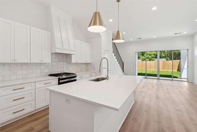 kitchen with pendant lighting, a kitchen island with sink, light hardwood / wood-style floors, white cabinetry, and stainless steel range with gas stovetop