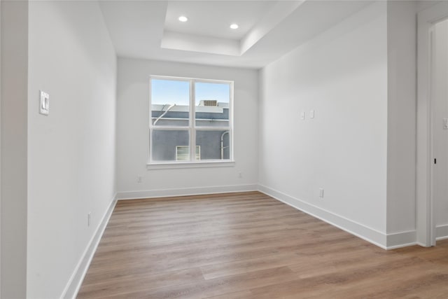 spare room with a raised ceiling and light hardwood / wood-style flooring