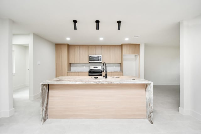 kitchen featuring a center island with sink, light brown cabinets, light stone counters, and appliances with stainless steel finishes