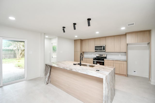 kitchen with light brown cabinetry, light stone counters, stainless steel appliances, sink, and an island with sink