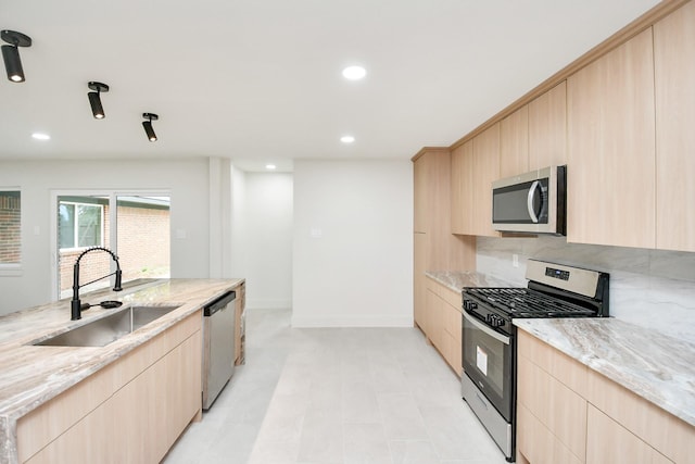 kitchen with light brown cabinetry, stainless steel appliances, light stone counters, and sink