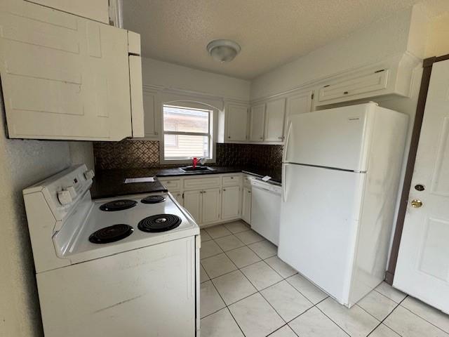 kitchen featuring decorative backsplash, white appliances, sink, light tile patterned floors, and white cabinetry