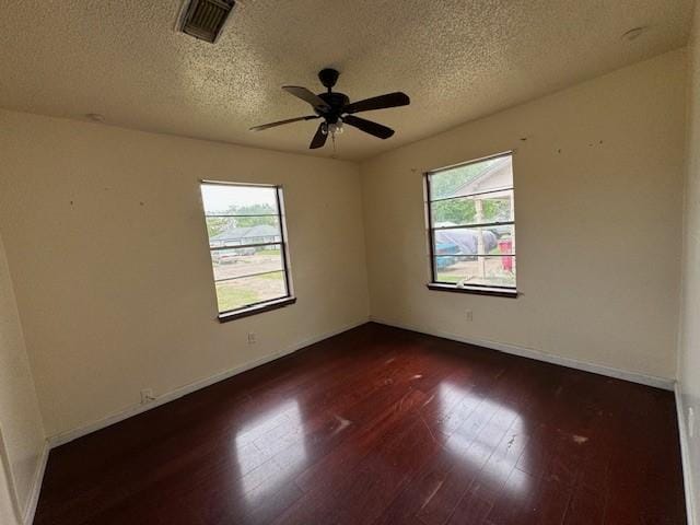 empty room featuring plenty of natural light, dark wood-type flooring, and a textured ceiling