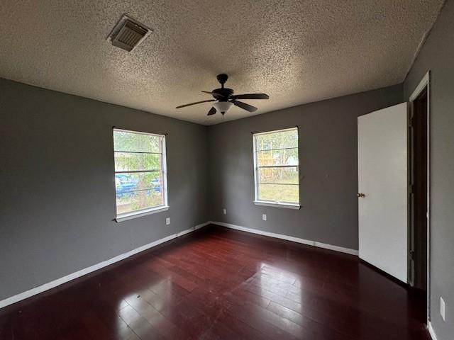 empty room featuring ceiling fan, dark hardwood / wood-style flooring, a healthy amount of sunlight, and a textured ceiling