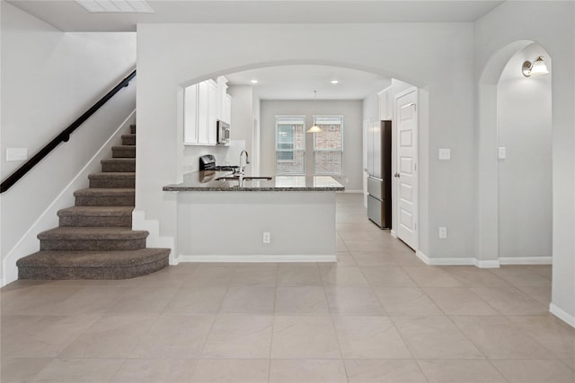 kitchen with kitchen peninsula, dark stone counters, stainless steel appliances, decorative light fixtures, and white cabinets