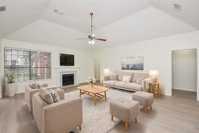 living room featuring ceiling fan, a fireplace, lofted ceiling, and light wood-type flooring