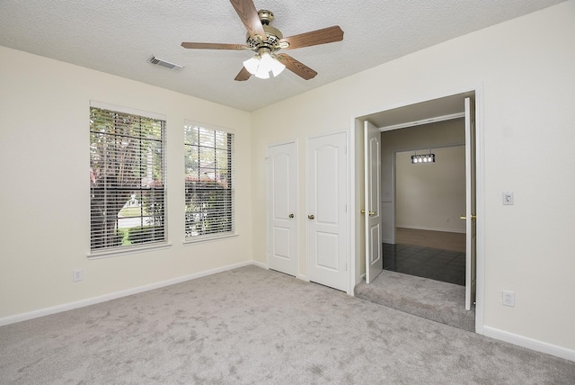 unfurnished bedroom with ceiling fan, light colored carpet, and a textured ceiling