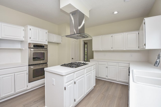 kitchen with island exhaust hood, stainless steel appliances, light hardwood / wood-style flooring, white cabinets, and a kitchen island