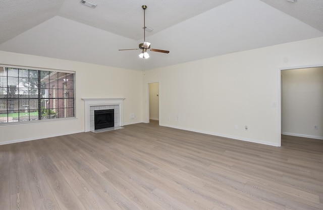 unfurnished living room with lofted ceiling, ceiling fan, light wood-type flooring, and a tile fireplace