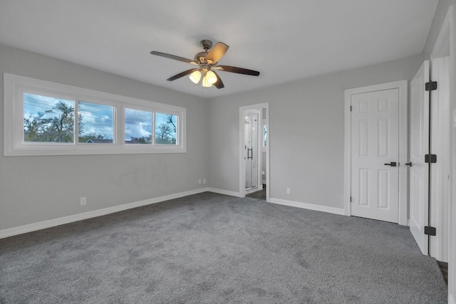 unfurnished bedroom with dark colored carpet, ensuite bath, and ceiling fan