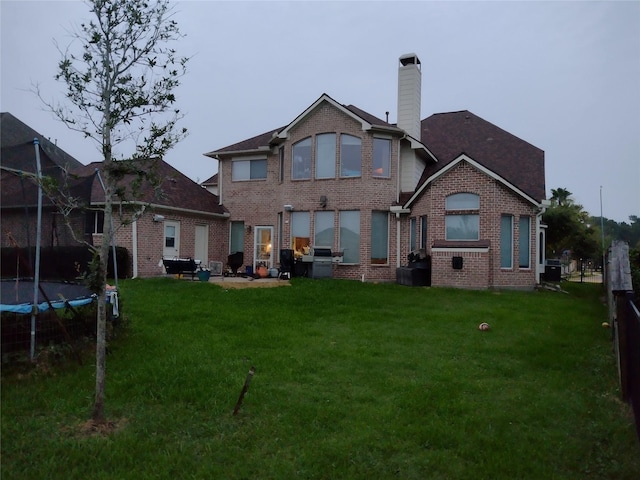 rear view of house featuring a trampoline and a lawn