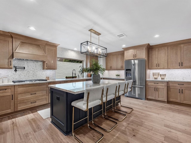 kitchen with premium range hood, light hardwood / wood-style floors, a kitchen bar, a kitchen island, and appliances with stainless steel finishes