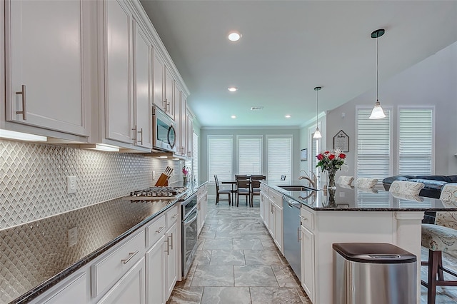 kitchen featuring a center island with sink, sink, appliances with stainless steel finishes, white cabinetry, and a breakfast bar area