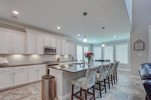 kitchen with a center island with sink, white cabinets, crown molding, hanging light fixtures, and stainless steel appliances