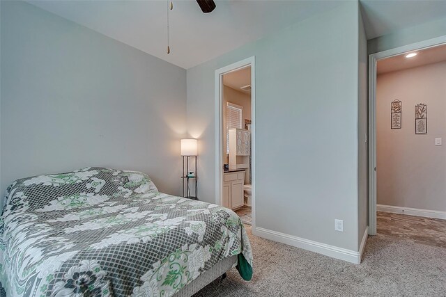 bedroom with ceiling fan, light colored carpet, and ensuite bath