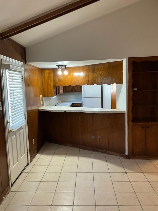 kitchen featuring kitchen peninsula, white refrigerator, wood walls, vaulted ceiling with beams, and light tile patterned flooring