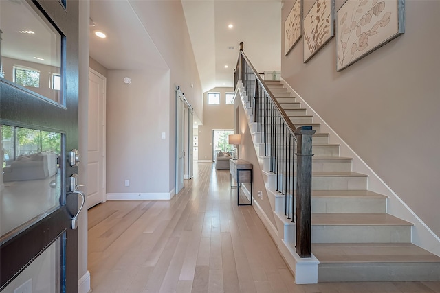 foyer featuring plenty of natural light, a barn door, light wood-type flooring, and high vaulted ceiling