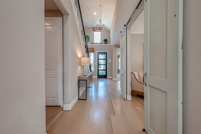 entrance foyer featuring a barn door, light hardwood / wood-style flooring, high vaulted ceiling, and a notable chandelier