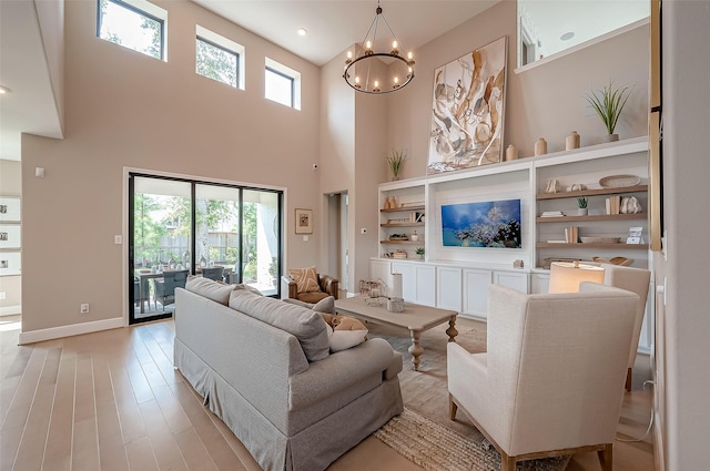 living room featuring plenty of natural light, light hardwood / wood-style floors, a high ceiling, and an inviting chandelier