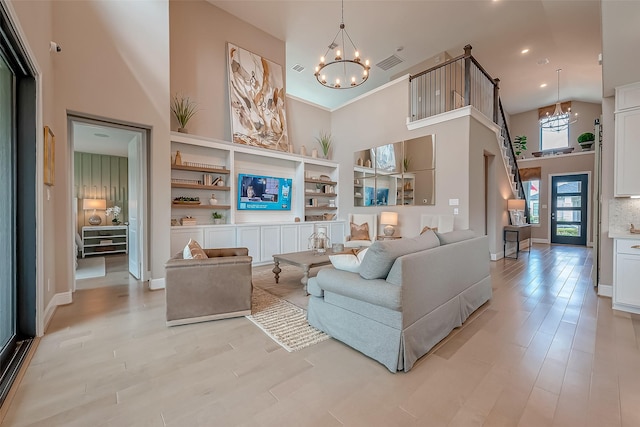 living room with light wood-type flooring, a towering ceiling, and an inviting chandelier