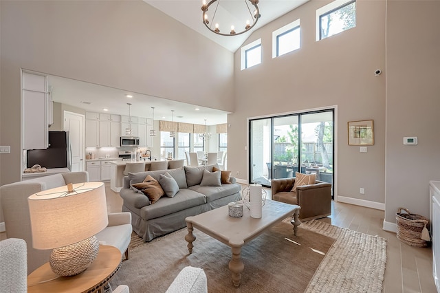 living room featuring a notable chandelier, light wood-type flooring, a high ceiling, and a wealth of natural light