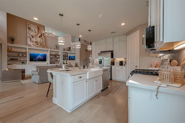 kitchen featuring appliances with stainless steel finishes, sink, white cabinets, hanging light fixtures, and an island with sink