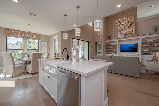 kitchen with white cabinetry, light hardwood / wood-style flooring, stainless steel dishwasher, pendant lighting, and a center island with sink