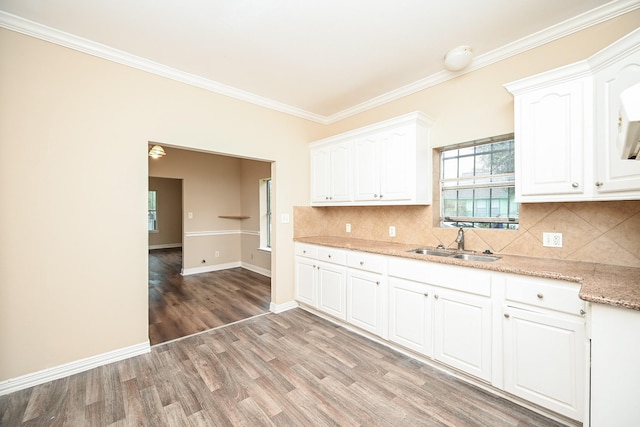 kitchen with sink, backsplash, wood-type flooring, white cabinets, and ornamental molding