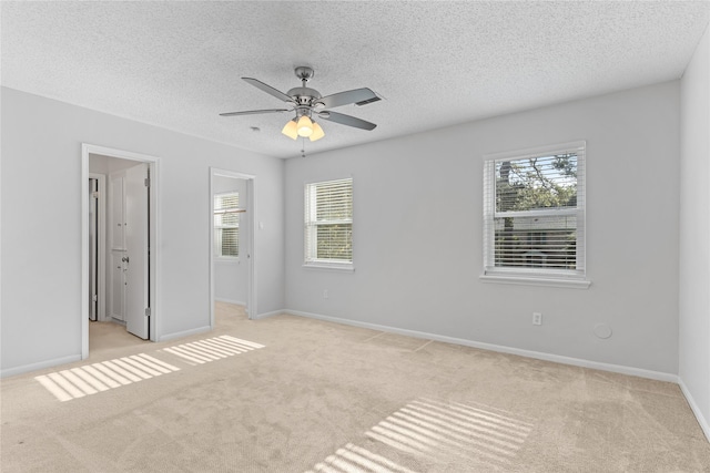 unfurnished bedroom featuring light carpet, a textured ceiling, multiple windows, and ceiling fan