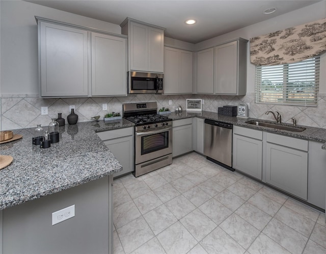 kitchen featuring gray cabinetry, sink, decorative backsplash, dark stone countertops, and appliances with stainless steel finishes