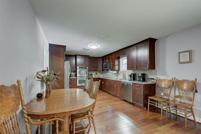 kitchen with dark brown cabinetry, sink, light hardwood / wood-style flooring, and appliances with stainless steel finishes